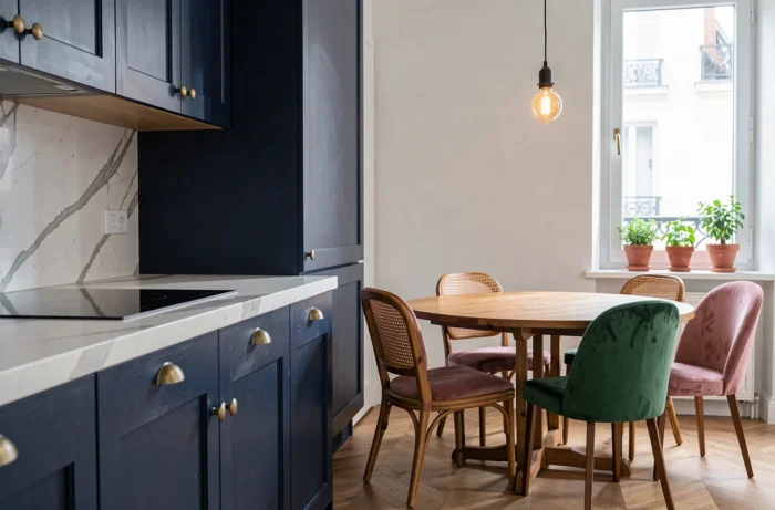 Cuisine ouverte moderne avec armoires bleu marine, plan de travail en marbre blanc et table ronde en chêne entourée de chaises vintage dépareillées